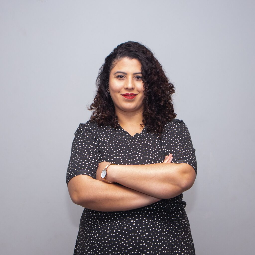 Portrait of a smiling woman in a polka dot dress with crossed arms against a gray background.
