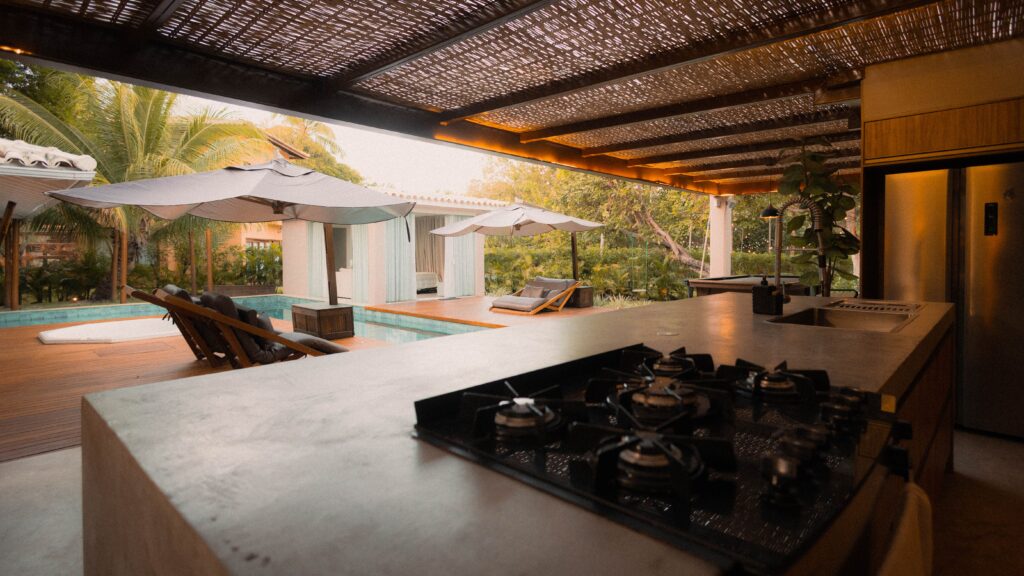 Modern outdoor kitchen overlooking a poolside setting at sunset, featuring elegant design and tropical ambiance.