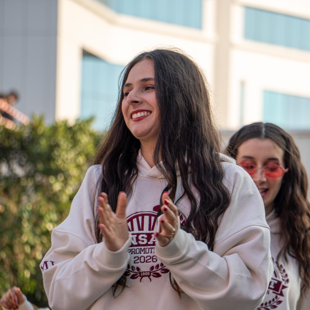 Two young women outdoor, clapping and smiling, enjoying a sunny day together.