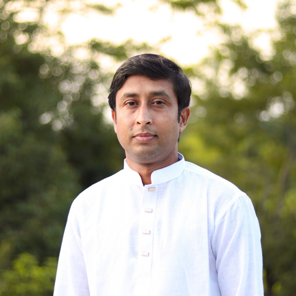 A serene portrait of an adult male outdoors in traditional white clothing, surrounded by lush greenery.